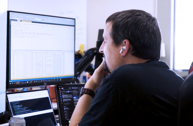 A man using technology to manage insurance policies from his desk with dual monitors.